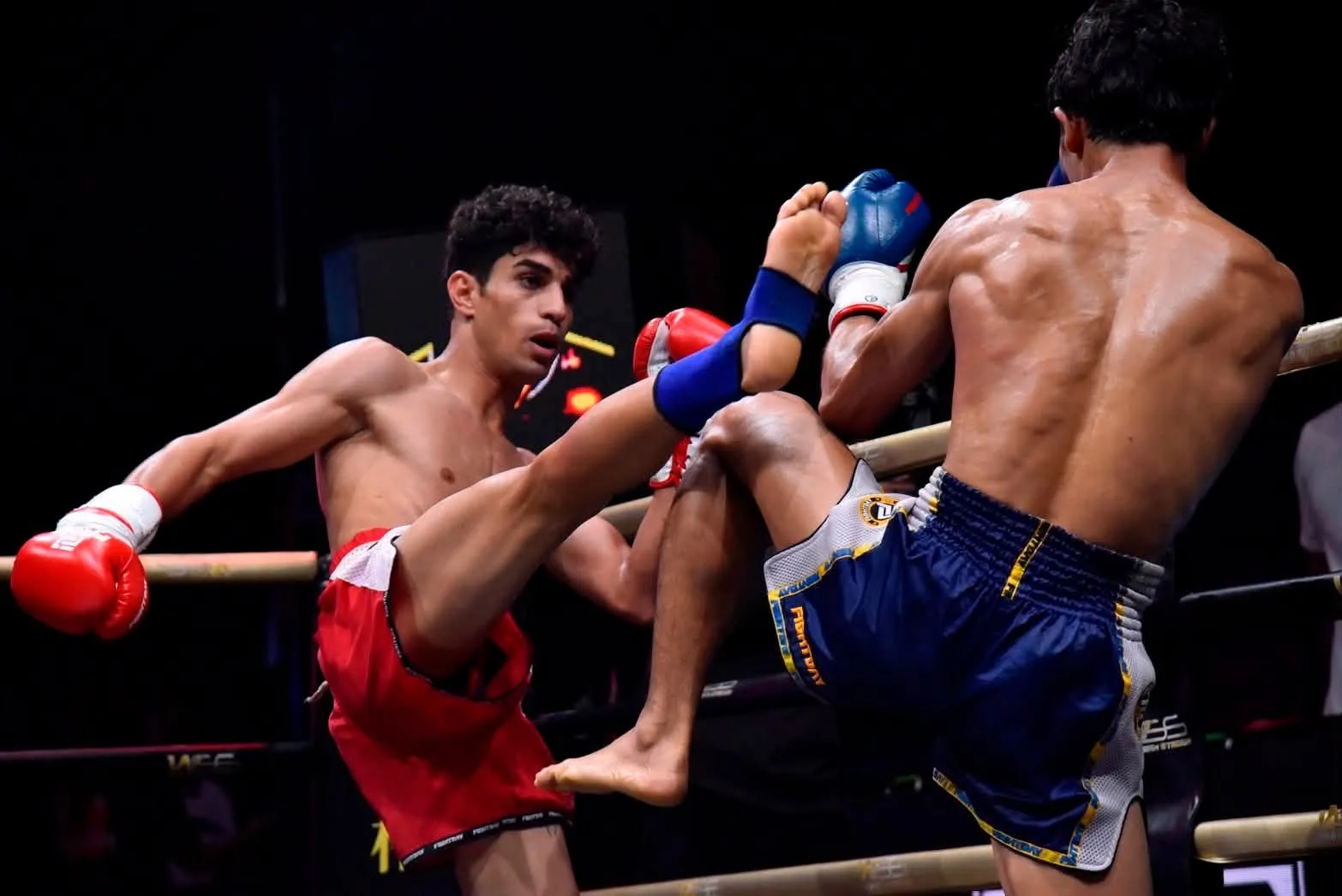 A Muay Thai fighter lands a high kick near the ropes